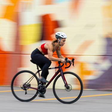 Woman cycling at high speed in front of a colorful graffiti wall, wearing athletic gear and a helmet. 